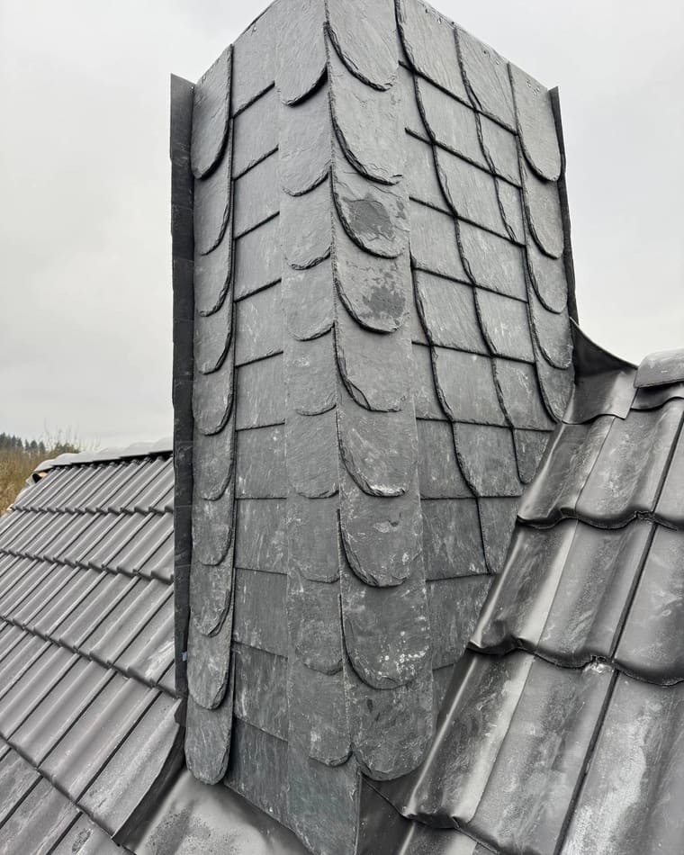 Mit Naturschiefer verkleideter Kamin auf einem grauen Ziegeldach